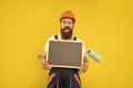 happy man housepainter in helmet and work clothes hold paint roller brush and blackboard