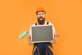 happy man housepainter in helmet and work clothes hold paint roller brush and blackboard