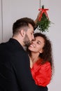 Happy man kissing his girlfriend under mistletoe bunch near light grey wall Royalty Free Stock Photo