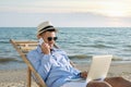 Happy man with laptop talking by mobile phone on beach. Business trip Royalty Free Stock Photo