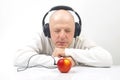 Happy man in light clothes wearing portable full-size headphones listens to music using an apple player Royalty Free Stock Photo