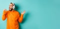 Happy man lipsync while listening music in headphones, holding invisible microphone, standing over turquoise background Royalty Free Stock Photo