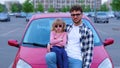 Happy man and little female kid in eyeglasses posing near red car on the parking while showing thumb up together. Family Royalty Free Stock Photo