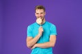 Happy man with lollipop on violet background. Macho smile with candy on stick on purple backdrop. Fashion model in blue tshirt wit
