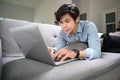 Happy man lying on sofa in living room and surfing internet with computer laptop. Royalty Free Stock Photo