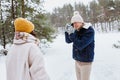 happy man photographing woman in winter forest