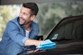 Happy man polishing car with microfiber cleaning cloth