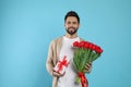Happy man with red tulip bouquet and gift box on light blue background. 8th of March celebration Royalty Free Stock Photo