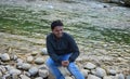 A happy man relaxing by mountain river enjoying natural landscape. Traveler backpacker sitting on rock on the Mangde chhu river Royalty Free Stock Photo