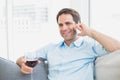 Happy man relaxing on sofa with glass of red wine talking on phone Royalty Free Stock Photo