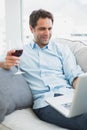 Happy man relaxing on sofa with glass of red wine using laptop Royalty Free Stock Photo
