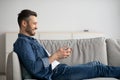 Happy man resting on couch at home, using modern smartphone