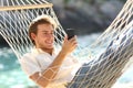 Happy man resting on a hammock using a smart phone