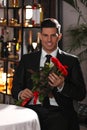 Happy man with roses waiting for his girlfriend in restaurant on Valentine`s day Royalty Free Stock Photo