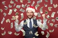 Happy man in Santa hat standing under money rain against red wall background Royalty Free Stock Photo