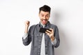 Happy man shouting yes, winning video game on mobile phone and triumphing, achieve online goal, standing on white Royalty Free Stock Photo