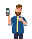 Happy man showing / holding credit / debit card and POS terminal payment card swipe machine and gesturing thumbs up sign. Royalty Free Stock Photo