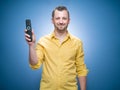 Happy man showing remote control, ready for watching TV - movies over blue background, dresses in yellow shirt. Its weekend.Front Royalty Free Stock Photo