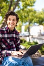 Happy man sitting on bench and using laptop in a park. Young man sitting on the park bench with laptop Royalty Free Stock Photo