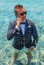 Happy man in a suit with a bow tie speaks on the phone at sea. Summer vacation concept