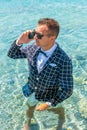 Happy man in a suit with a bow tie speaks on the phone at sea. Summer vacation concept