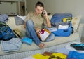 Happy man talking on mobile phone holding passport packing travel suitcase organizing clothes and things getting ready for summer Royalty Free Stock Photo