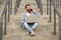 Happy man talking on mobile phone working on laptop. Smiling man making mobile call on stairs Royalty Free Stock Photo