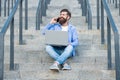 Happy man talking on mobile phone working on laptop. Smiling man making mobile call on stairs Royalty Free Stock Photo