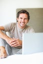 Happy man using laptop in bed. Portrait of handsome man sitting with laptop on bed.