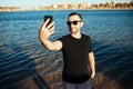 Happy young man on vacation laughing at the beach taking selfie in sunglasses on sea background Royalty Free Stock Photo