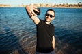 Happy young man on vacation laughing at the beach taking selfie in sunglasses on sea background Royalty Free Stock Photo