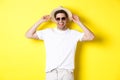 Happy man on vacation, wearing straw hat and sunglasses, smiling while standing against yellow background Royalty Free Stock Photo