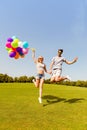 Happy man and woman holding balloons and jumping in the park Royalty Free Stock Photo
