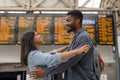 Happy man and woman in love meet and cuddle at train station in front of the timetable Royalty Free Stock Photo