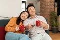 Happy married asian couple spending time at home together, drinking coffee and watching tv, relaxing on couch Royalty Free Stock Photo