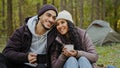Happy married couple drinking hot drink outdoors in autumn forest young hikers resting in nature at campsite people in Royalty Free Stock Photo
