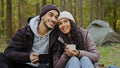 Happy married couple drinking hot drink outdoors in autumn forest young hikers resting in nature at campsite people in Royalty Free Stock Photo