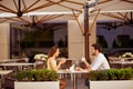 Happy married couple is on a honey moon, having brunch in nice cafe with modern interior, light summer terrace with green nice pla