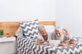 Happy married senior couple laughing together sitting in bed watching a fun video on tablet - Mature people having fun - Royalty Free Stock Photo