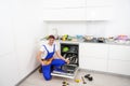 Happy master. Male technician sitting near dishwasher with screwdriver in kitchen with instruments and smiling