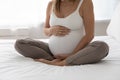 Pregnant woman sits cross-legged on bed touch belly enjoy pregnancy Royalty Free Stock Photo