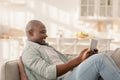 Happy mature african american man spending time with digital tablet at home, browsing internet while relaxing on sofa Royalty Free Stock Photo