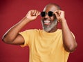 Happy mature african american man standing alone against a red background in a studio and posing with sunglasses Royalty Free Stock Photo