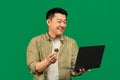 Happy mature asian man holding golden bitcoin and laptop, earning cryptocurrency, standing over green background