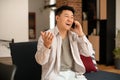 Happy mature asian man talking on cellphone and gesturing, having pleasant conversation while sitting on sofa at home Royalty Free Stock Photo