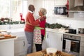 Happy mature black couple holding champagne glasses, laughing and embracing in the kitchen while preparing meal on Christmas morni Royalty Free Stock Photo