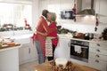 Happy mature black couple holding champagne glasses, laughing and embracing in the kitchen while preparing meal on Christmas morni Royalty Free Stock Photo