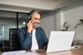 Happy mature business man talking on cell phone working on laptop in office. Royalty Free Stock Photo