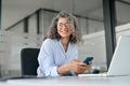 Happy mature business woman holding mobile phone looking away in office. Royalty Free Stock Photo