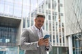 Happy mature businessman in suit using mobile phone standing outdoors. Royalty Free Stock Photo